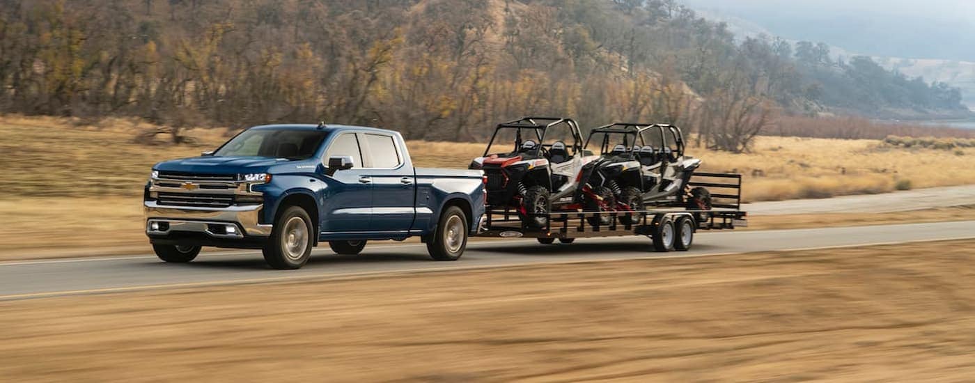 A blue 2020 Certified Pre-Owned Chevy Silverado 1500 towing ATVs on a trailer.