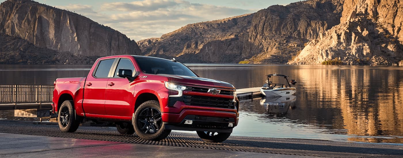 A red 2024 Chevy Silverado 1500 LTZ Z71 parked at a boat launch next to a lake.