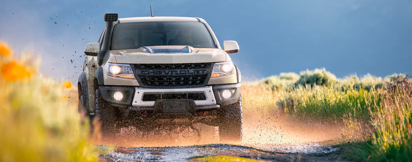 A tan 2022 Chevy Colorado ZR2 Bison kicking up mud on a trail while off-roading.