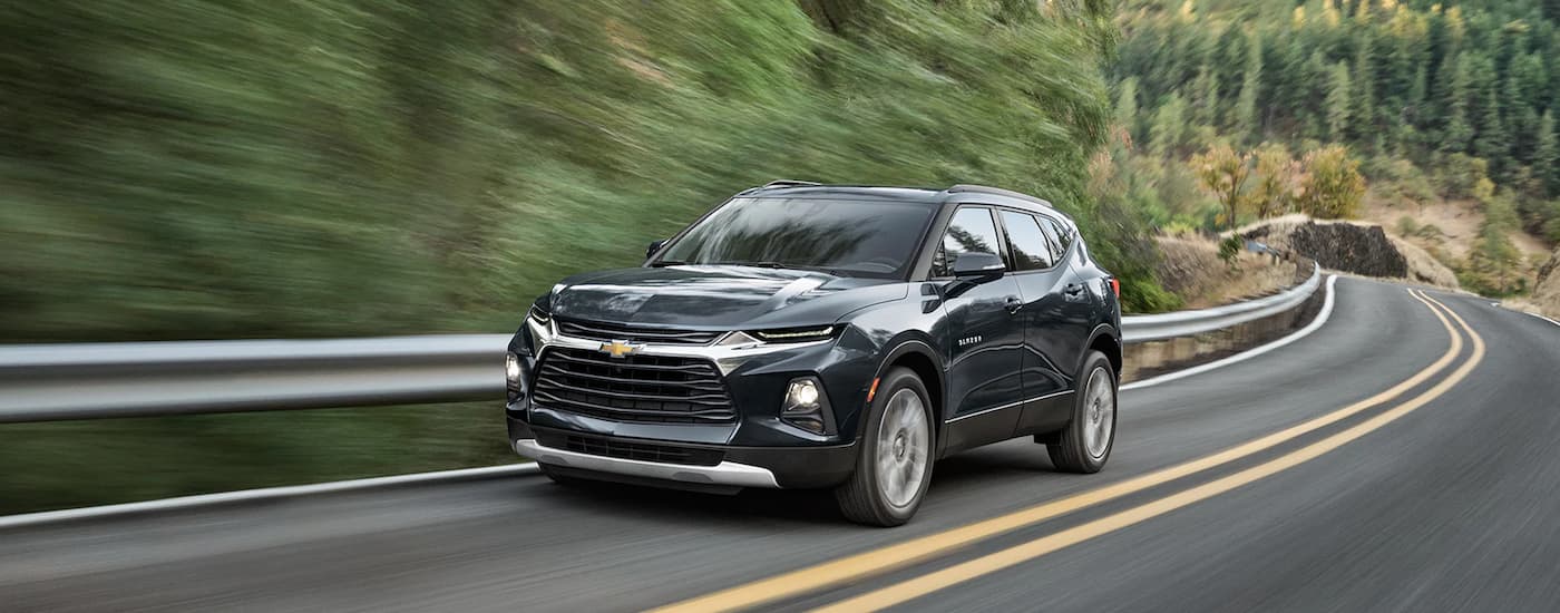 A black 2022 Chevy Blazer is shown driving on a road lined with trees.