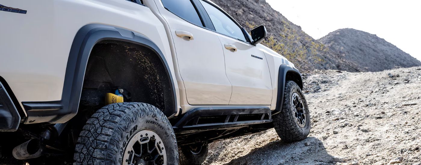 Low-angle rear view of a white 2025 Chevy Colorado TrailBoss off-roading up a mountain.