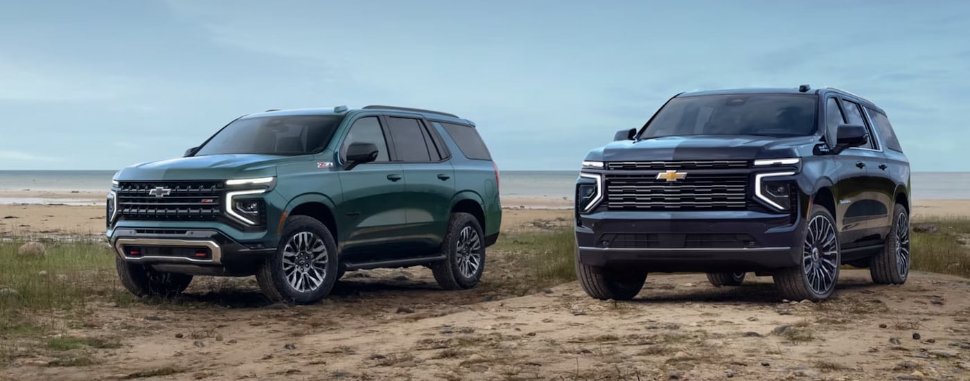 A teal 2025 Chevy Tahoe Z71 and blue 2025 Chevy Suburban High Country parked on a beach.
