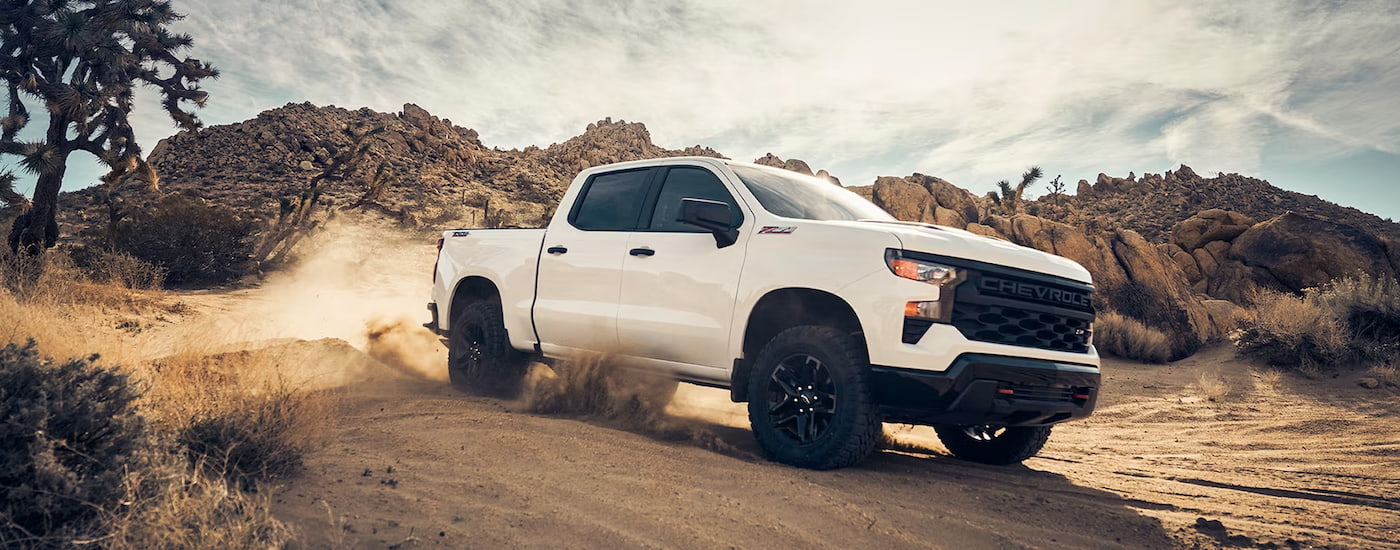 A white 2024 Chevy Silverado 1500 Custom Trail Boss kicking up sand while off-roading.