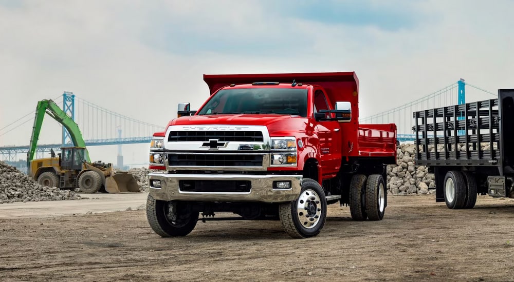 A red 2024 Chevy Silverado 6500 HD Chassis Cab dump truck at a construction site.