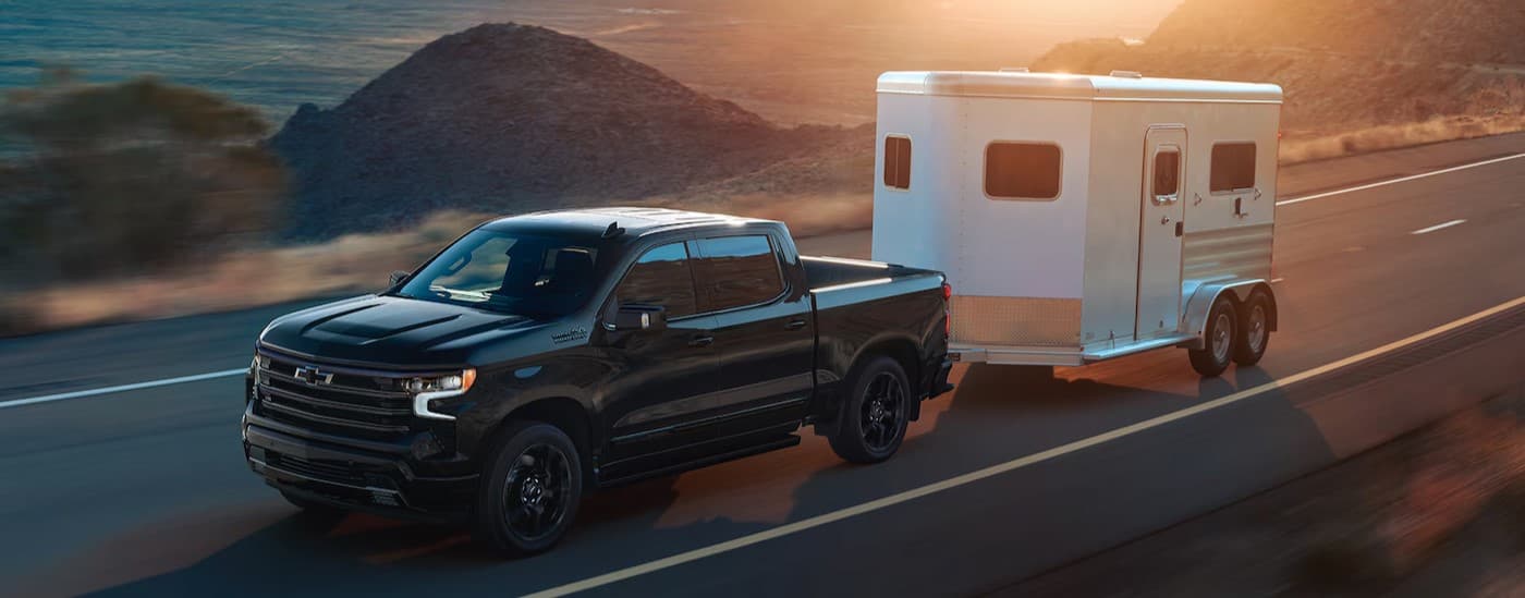 A black 2025 Chevy Silverado 1500 High Country Midnight Edition is shown towing a trailer.