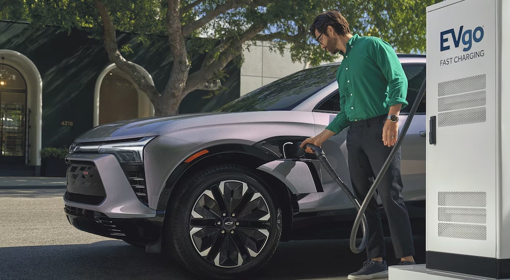 A man plugging in a silver 2024 Chevy Blazer EV RS for fast charging at a public charging station.