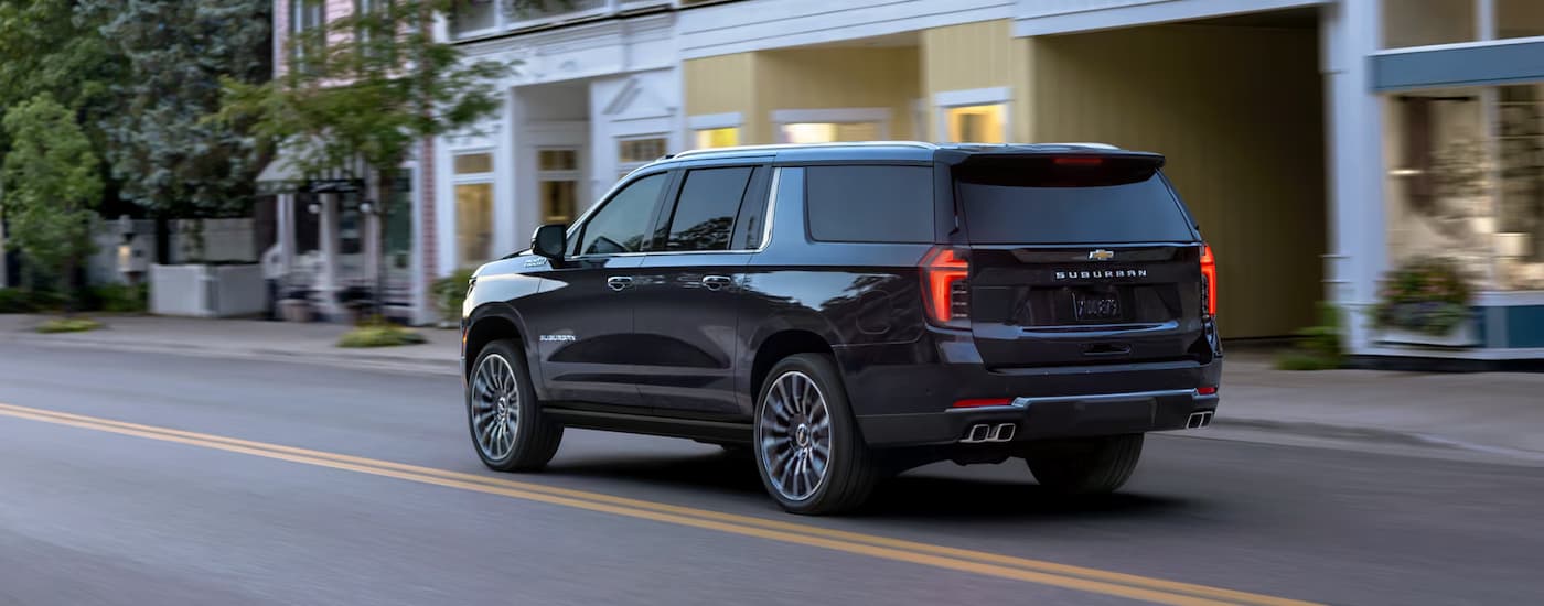 A black 2025 Chevy Suburban High Country driving through a city center.
