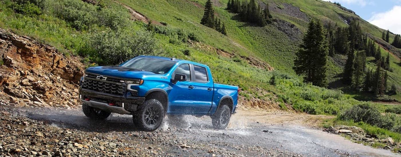 A blue 2024 Chevy Silverado 1500 ZR2 is shown from the front while driving through a creek.