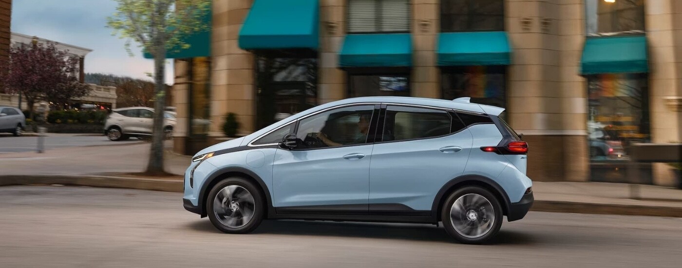A blue 2023 Chevy Bolt EV is shown from the side driving on a city street.