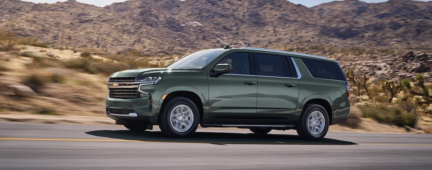 Side view of a green 2024 Chevy Suburban LT driving through the desert.