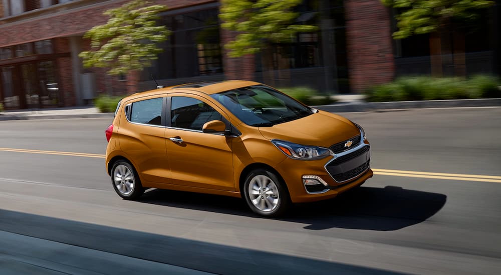 An orange 2020 Chevy Spark is shown driving on a city street after viewing used cars for sale in Sacramento.