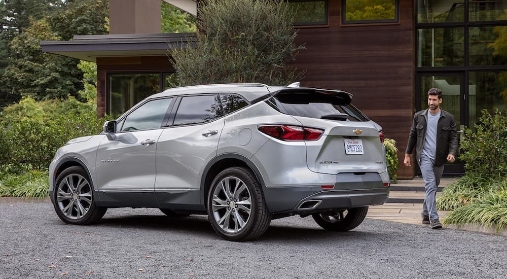 A grey 2022 Chevy Blazer is shown being approached by a person outside of a house.