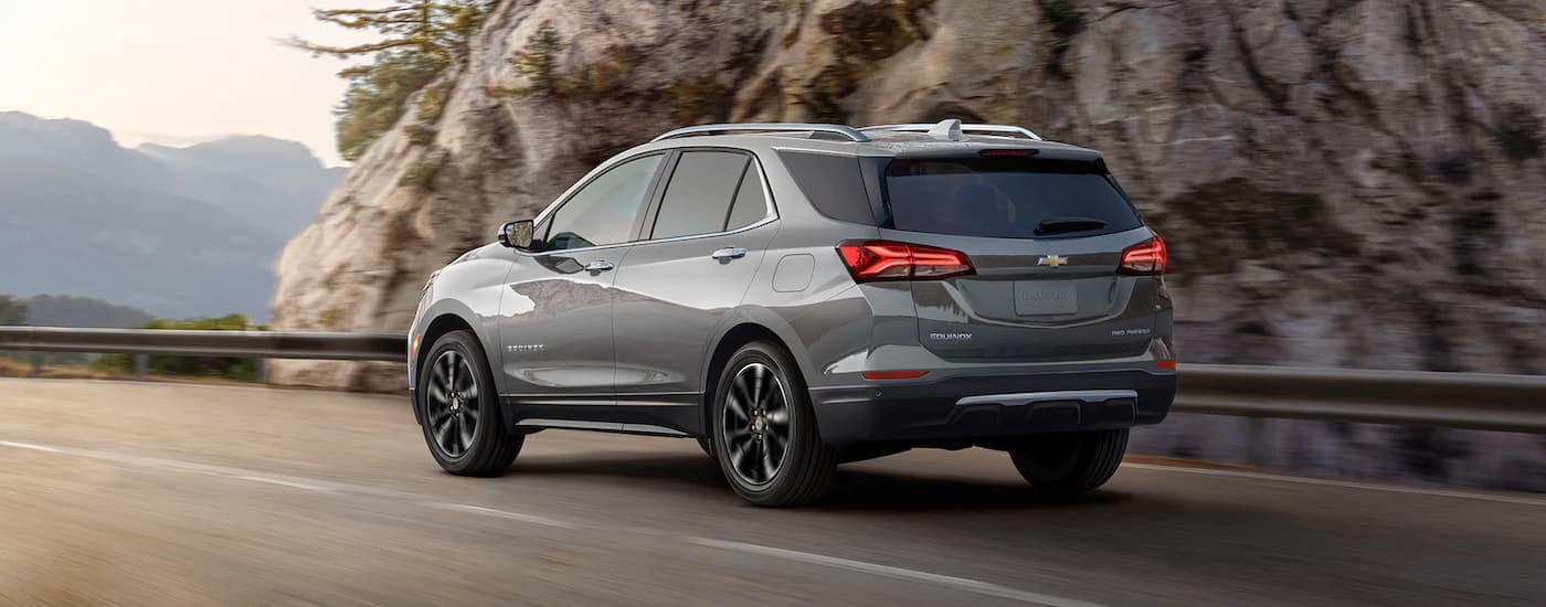 A grey 2023 Chevy Equinox is shown driving on a road through the mountains.