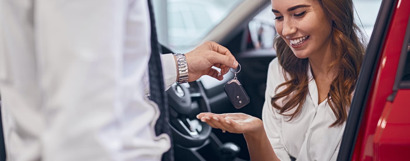 A salesman hands car keys to a smiling woman in a red vehicle.