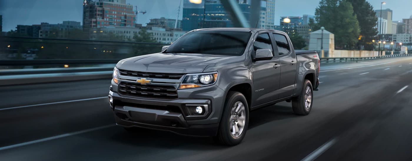 A grey 2022 Chevy Colorado is shown driving on a bridge at night.
