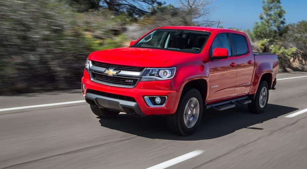 A red 2015 Chevy Colorado used truck for sale is shown driving on an open road during a test drive.