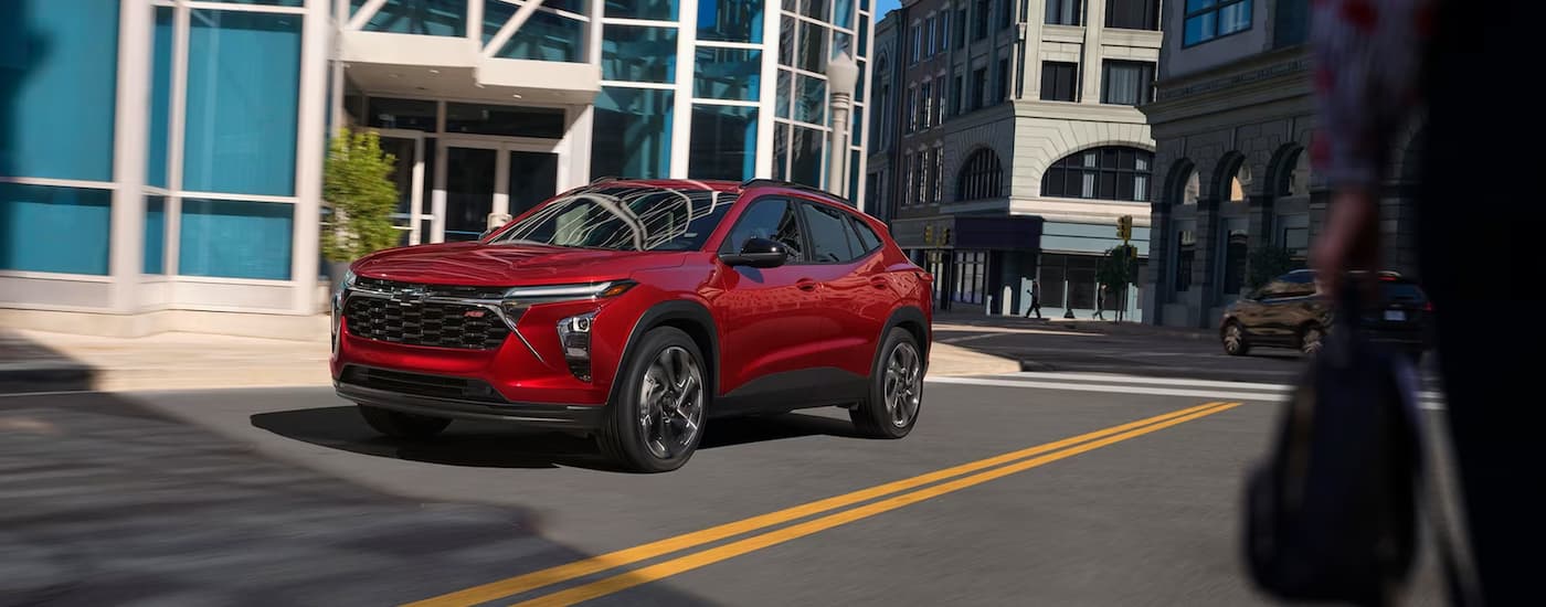 A 2024 Chevy Trax RS is shown driving on a city street during the day.