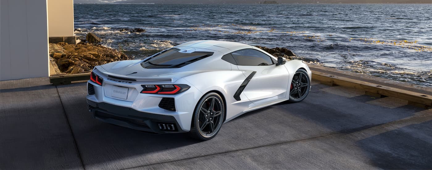 A white 2022 Chevy Corvette is shown parked next to a modern house on the coast.