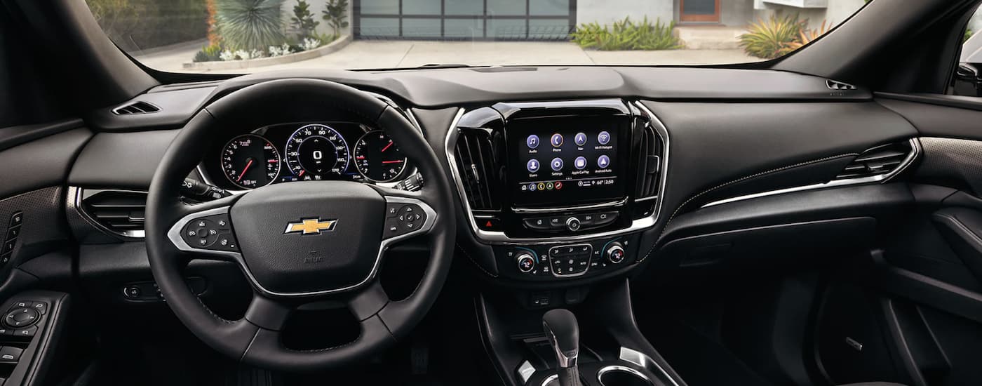 The black interior of a 2023 Chevy Traverse shows the steering wheel and infotainment screen.