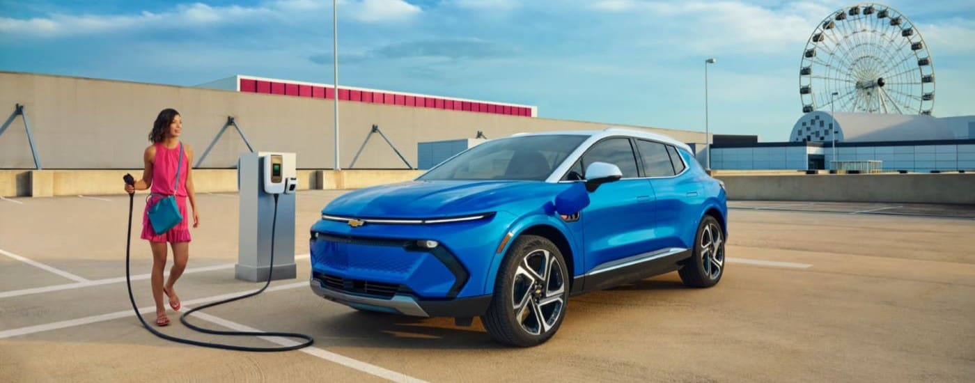 A blue 2024 Chevy Equinox EV is shown next to a person holding a charging cable.