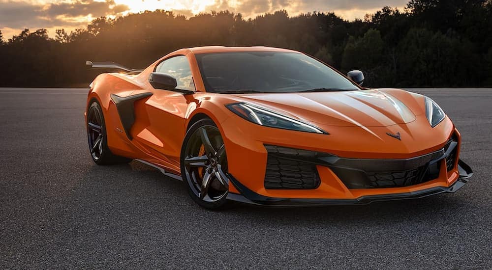 An orange 2022 Corvette Z06 in an empty parking lot with trees and the setting sun 
