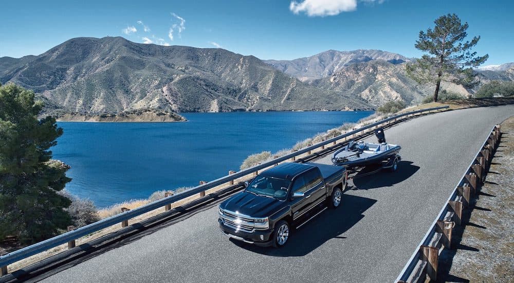 A black 2018 Chevy Silverado 1500 High Country is shown towing a boat near a lake.