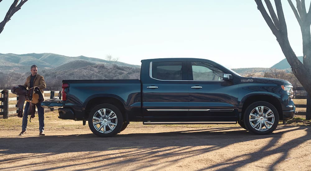 A man on a ranch loading a saddle into the bed of a dark blue 2022 Chevy Silverado 1500 High Country.