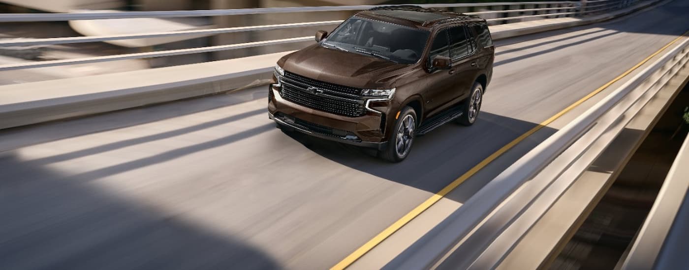 A brown 2023 Chevy Tahoe is shown driving on a highway after viewing a used Chevy for sale.