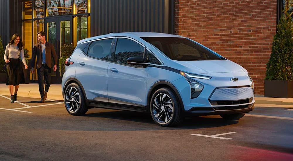 A light blue 2022 Chevy Bolt EV is shown parked near a couple walking.