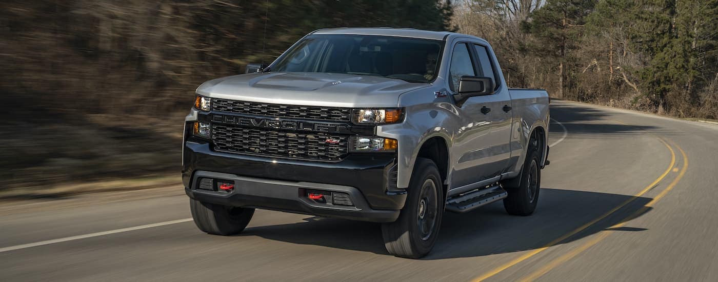 A silver 2020 Chevy Silverado 1500 Z71 Trail Boss driving on a wooded highway.