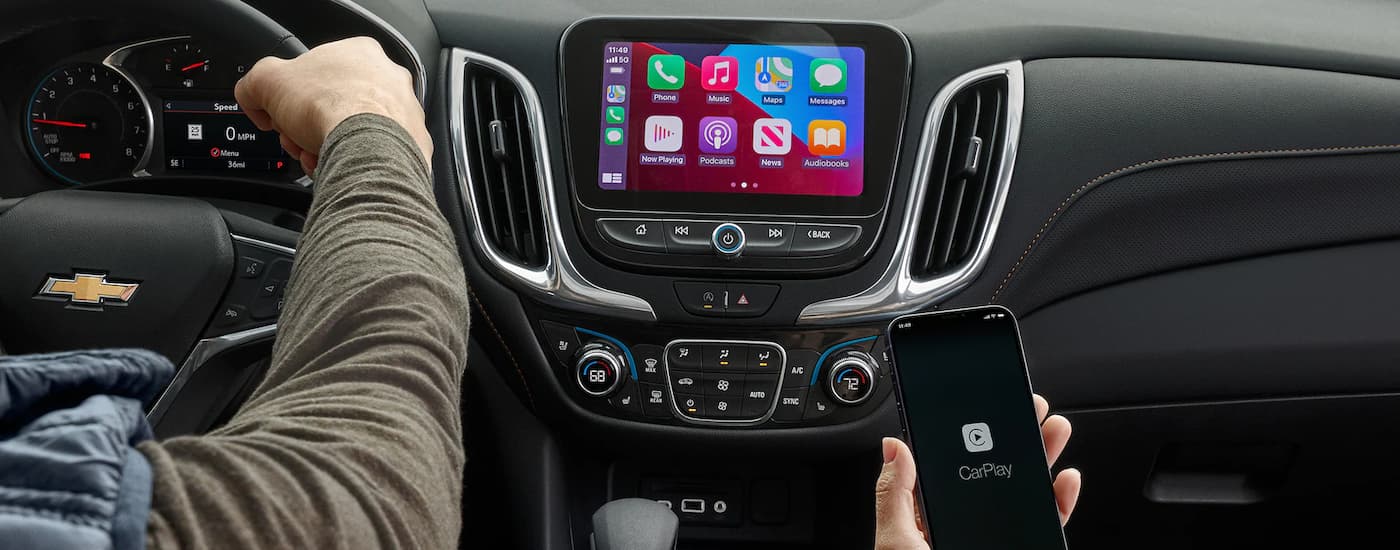 A close up shows Apple CarPlay on a phone and infotainment screen in a 2023 Chevy Equinox.