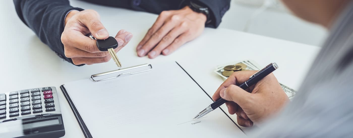 A buyer signing financing paperwork as the dealer hands over the key fob.