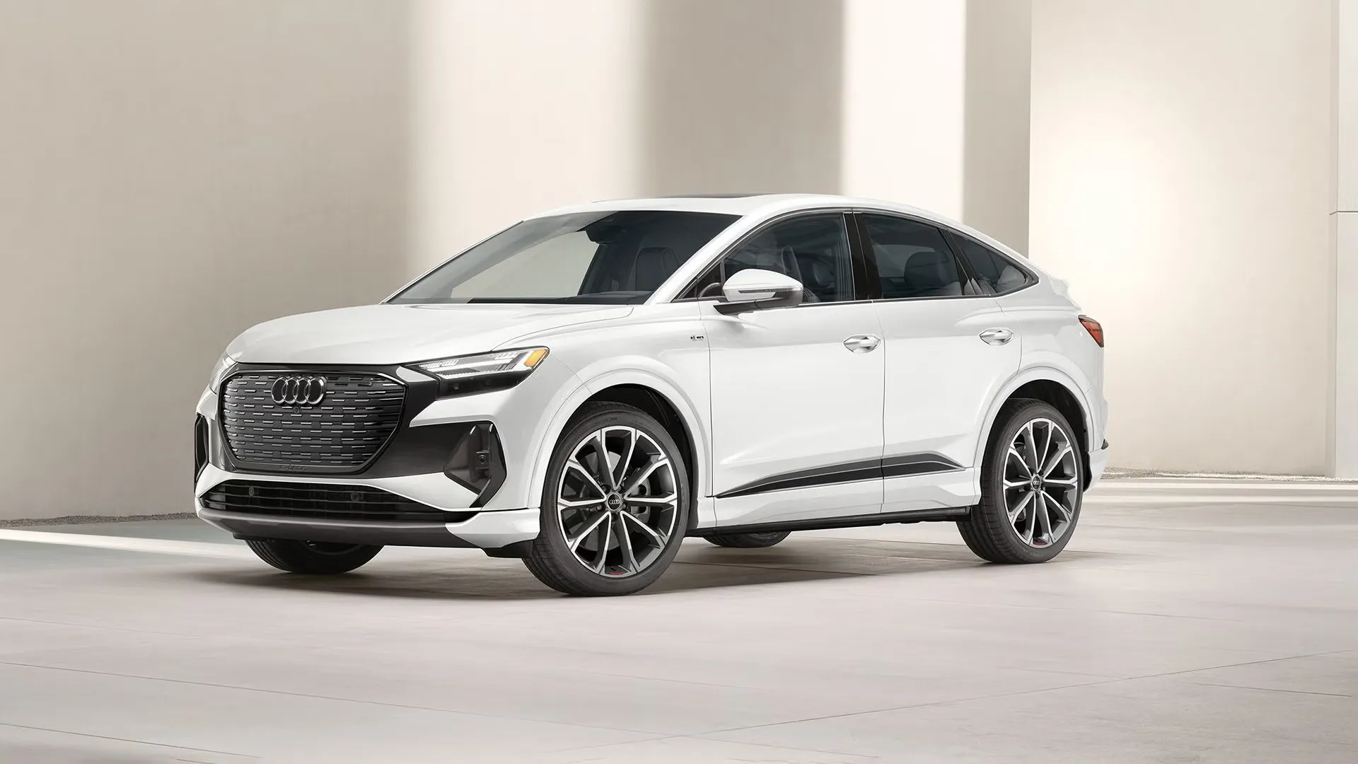 2025 white Audi Q4 Sportback e-tron parked in a minimalist setting with light walls and concrete floor.