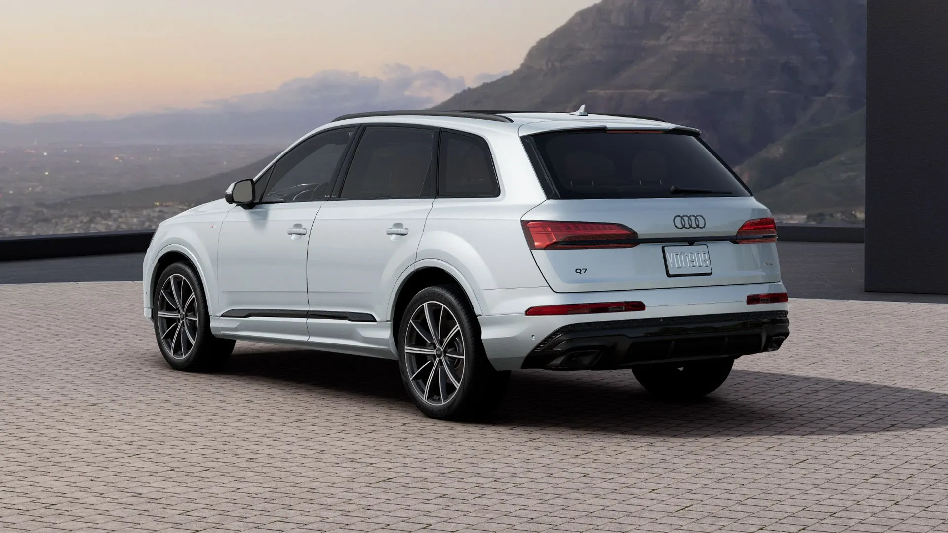 Vue trois quarts arrière de l’Audi Q7 2026 blanche stationnée sur une esplanade, mettant en valeur la signature lumineuse arrière et les lignes élégantes du VUS.