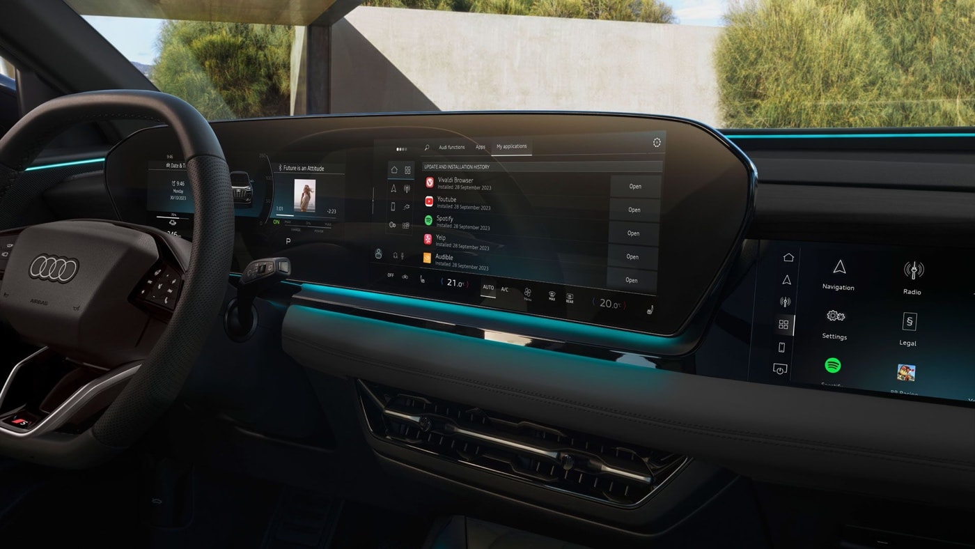 Vue intérieure du Audi Q6 e-tron avec large écran panoramique 14,5 pouces affichant Spotify et commandes numériques intégrées.