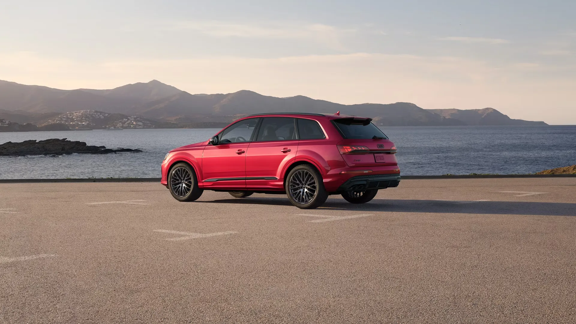 Vue trois quarts arrière de l’Audi SQ7 2026 rouge stationnée face à la mer, illustrant son design sportif et son allure haut de gamme dans un environnement côtier.