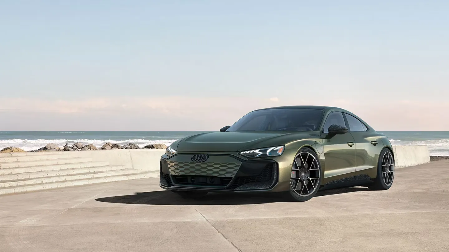 Audi RS e-tron GT 2025 vert olive stationnée devant l’océan, sur un trottoir bétonné près de la plage.