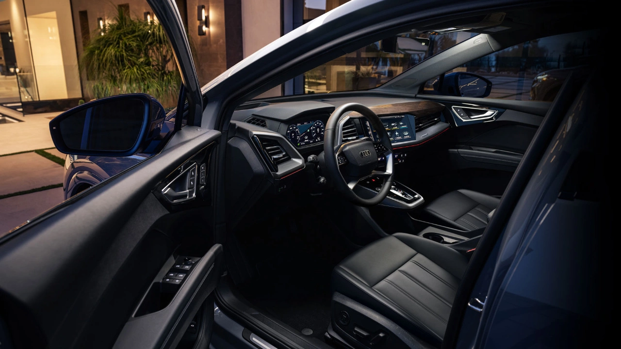 Interior view of the 2025 Audi Q4 e-tron with modern cabin, black upholstery, and illuminated digital dashboard at the entrance of a contemporary house.