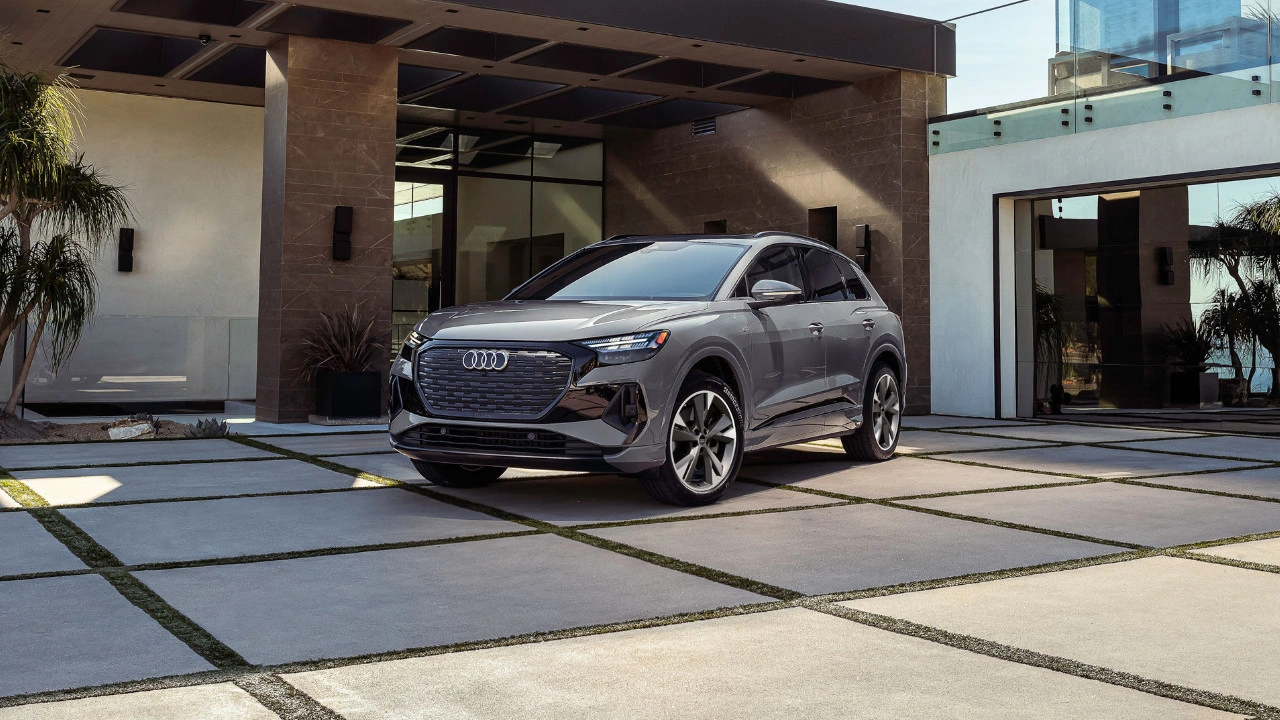 2025 grey Audi Q4 e-tron parked in a modern driveway in front of a luxury house with large windows and palm trees.