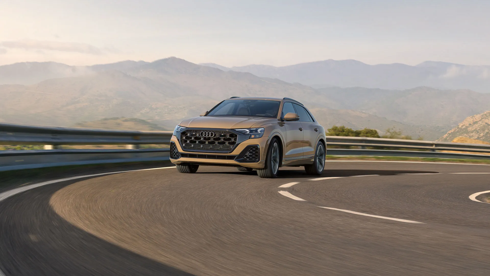 Audi Q8 2025 beige en virage sur route de montagne, démontrant la performance et la stabilité de la transmission intégrale.