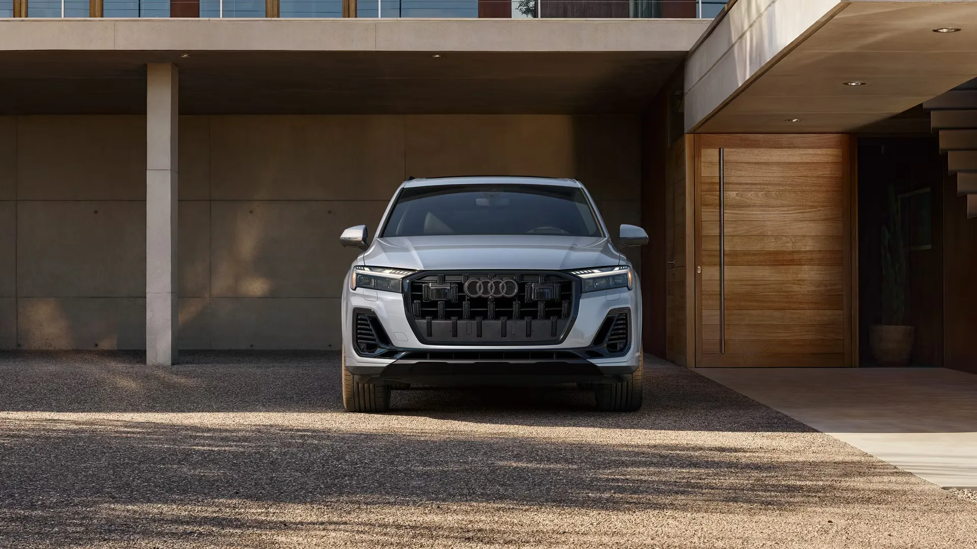 Vue avant de l’Audi Q7 2026 gris stationnée devant une maison moderne, mettant en valeur sa calandre octogonale revisitée et son design haut de gamme.