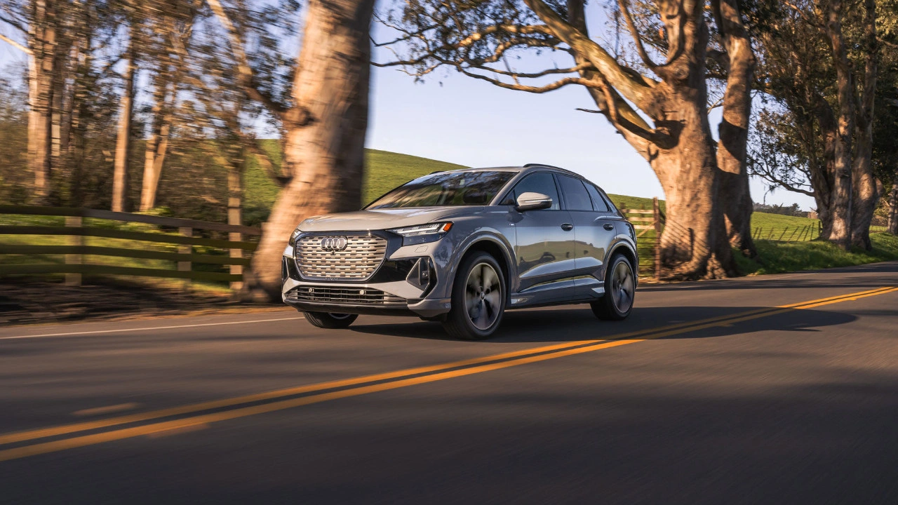2025 Audi Q4 e-tron grey three-quarter front left view driving on a tree-lined road.