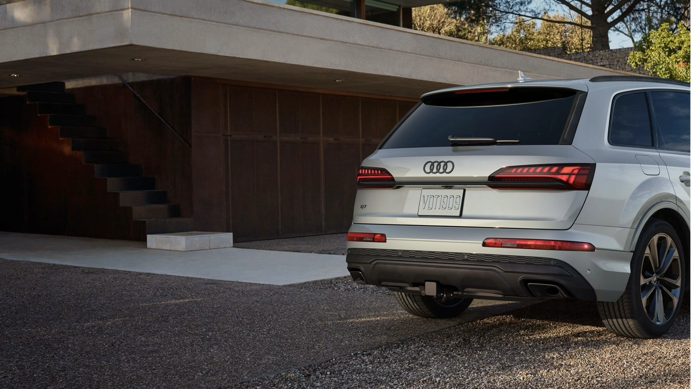 Vue arrière de l’Audi Q7 2025 argent stationné devant une maison moderne en béton, avec feux arrière à DEL allumés.