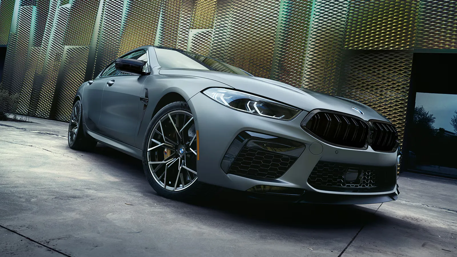 BMW M8 Competition Gran Coupé 2025 stationnée devant une façade dorée, vue en contre-plongée.