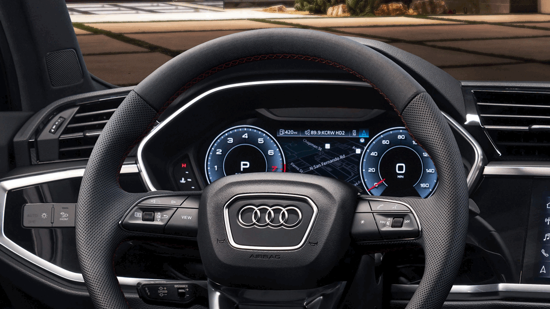 Close-up of the Audi Q3 2025 steering wheel with red stitching and Virtual Cockpit digital dashboard displaying navigation and gauges.