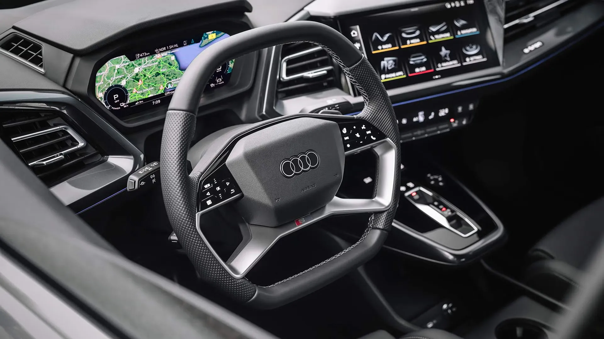 Close-up of the 2025 Audi Q4 Sportback e-tron multifunction sport steering wheel with Audi logo and digital display showing navigation.