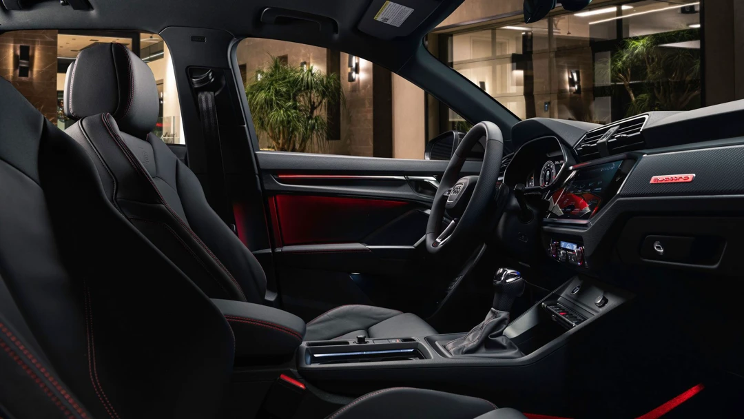 Interior of the 2025 Audi Q3 with black sport seats and red stitching, red ambient lighting, and a high-tech dashboard.