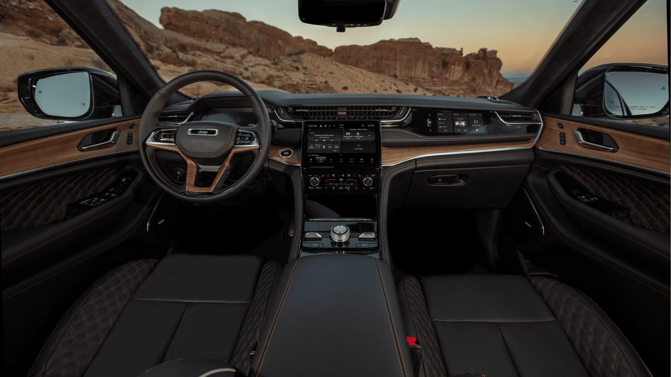 Luxurious interior of the 2025 Jeep® Grand Cherokee with a leather-wrapped steering wheel, digital displays, and scenic desert views.