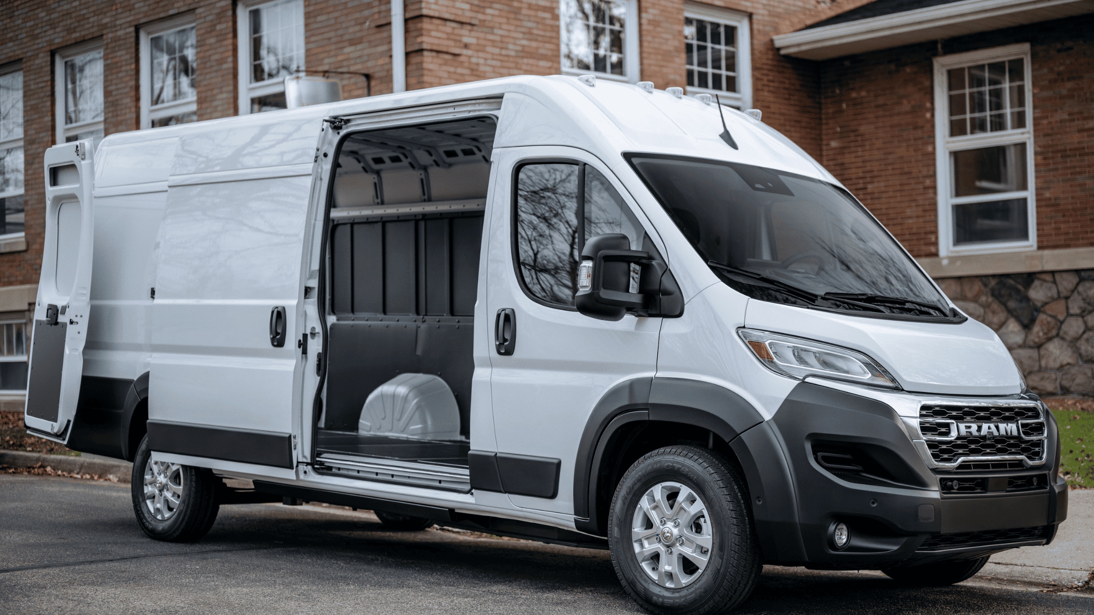 A white 2024 Ram ProMaster van parked on a residential street, with its side doors open to reveal a spacious and empty cargo area, ideal for commercial use.
