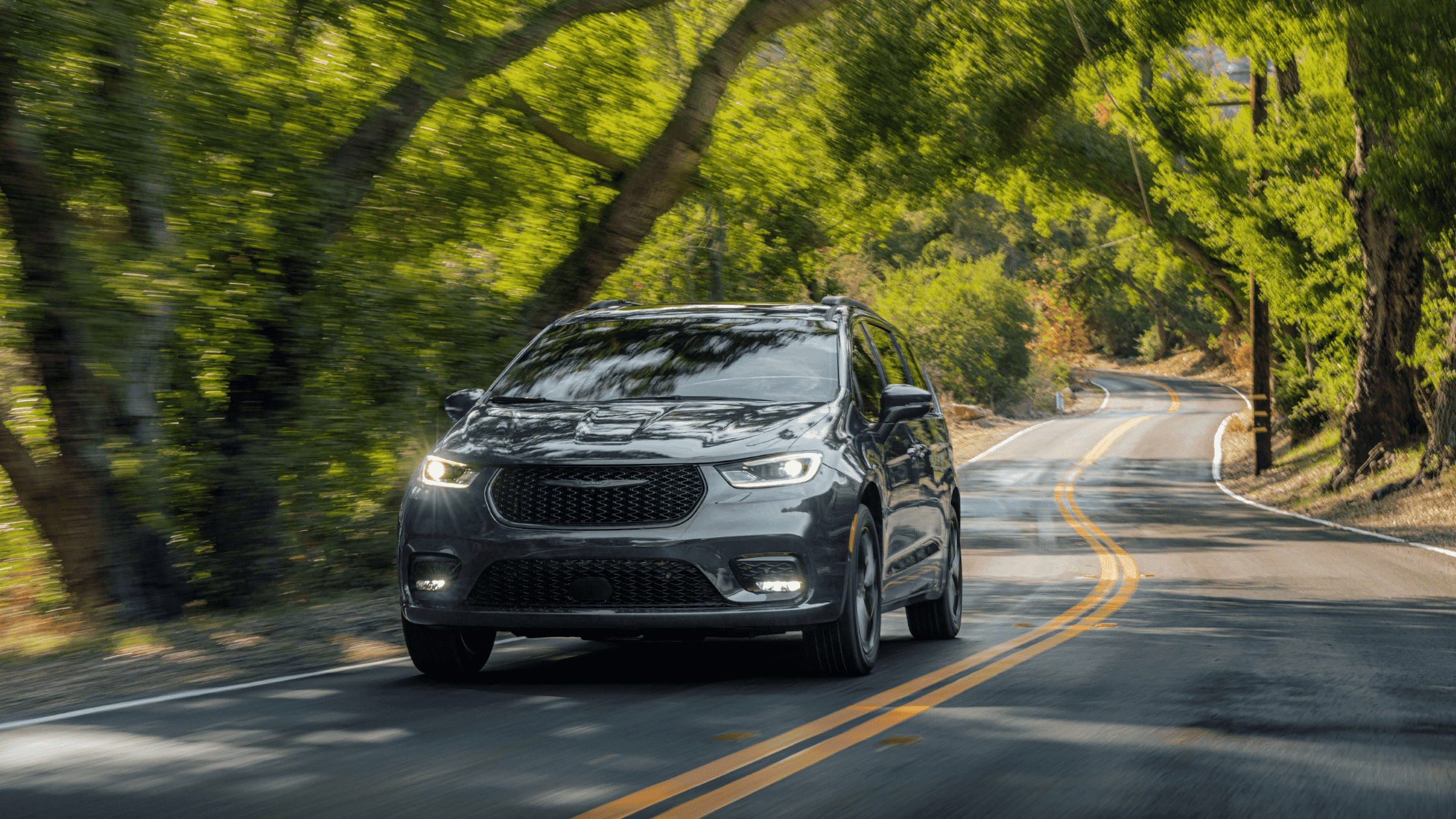 2024 Chrysler Pacifica driving on a scenic road near Naples, FL, showcasing its sleek design and family-friendly features ideal for long drives.